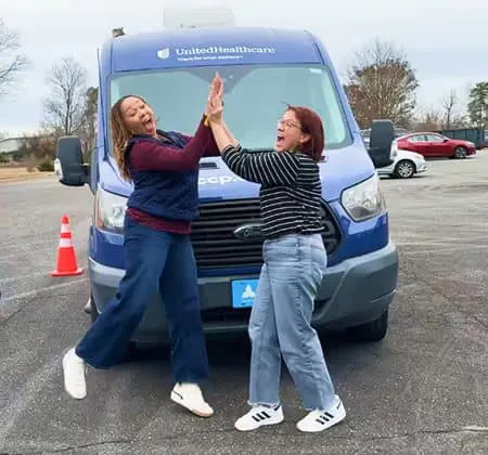 Two trainees high-fiving in front of a mobile clinic